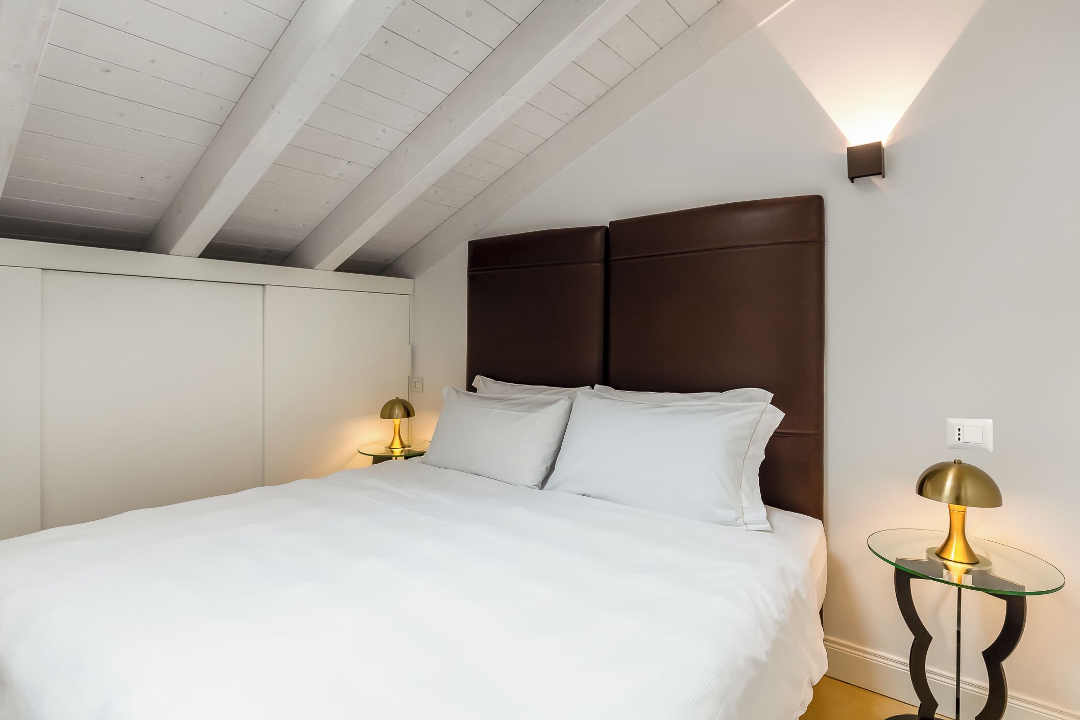 Un lit bien fait, avec du linge de lit blanc, une tête de lit en bois foncé et deux tables de chevet avec des lampes.