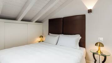 Un lit bien fait, avec du linge de lit blanc, une tête de lit en bois foncé et deux tables de chevet avec des lampes.
