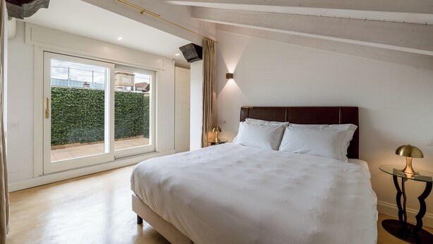 Un dormitorio con una cama grande, una mesita de cristal y vistas al balcón a través de un ventanal corredero.