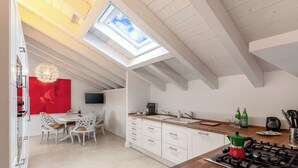 Una cocina moderna con tragaluz, armarios blancos, una zona de comedor con sillas blancas y una pared de acento roja.