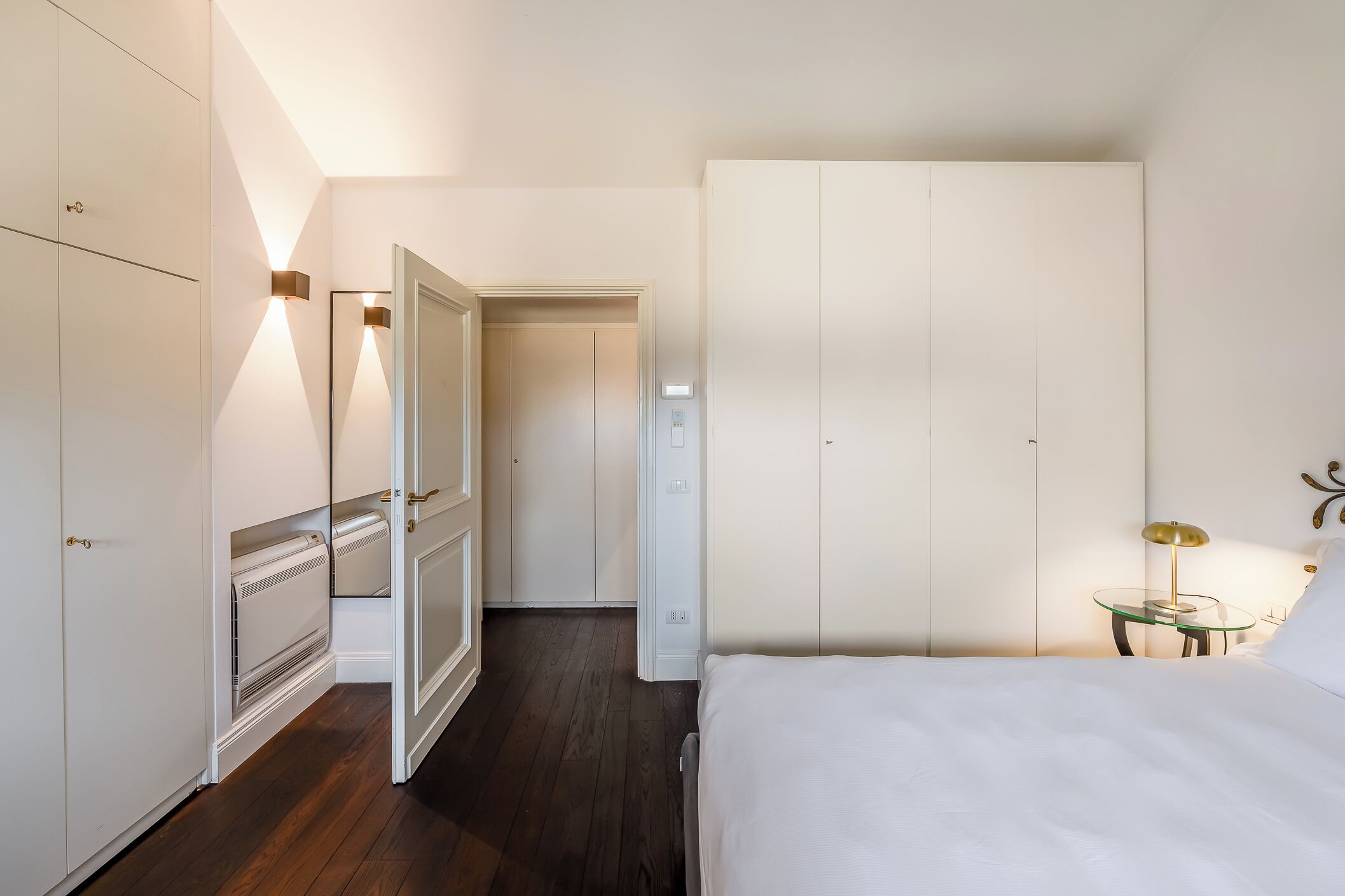 A bedroom with a bed, a wardrobe, a radiator, and a nightstand with a lamp.
