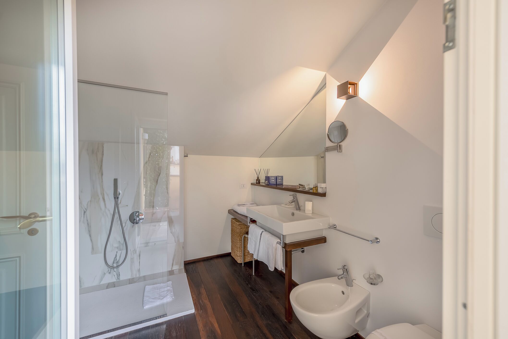 A modern bathroom with a glass shower enclosure, a white sink, and a bidet.