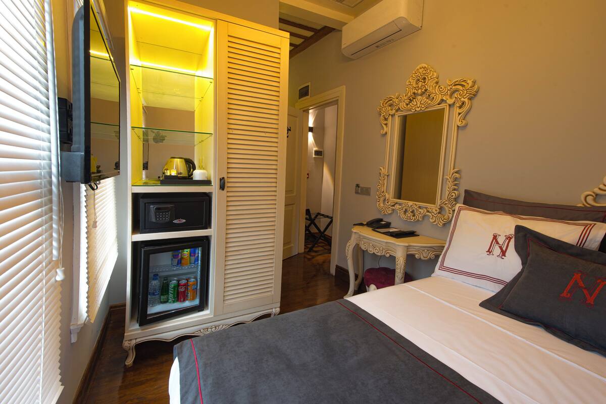A hotel room with a bed, a bedside table, a mirror, a wardrobe, and a minibar.