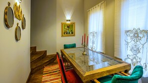 A dining area with a glass-top table, green upholstered chairs, a patterned rug, and a staircase with wooden steps. - NİA SULTANAHMET HOTEL (Istanbul)