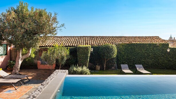 A swimming pool with clear water, surrounded by a tiled deck and lounge chairs.