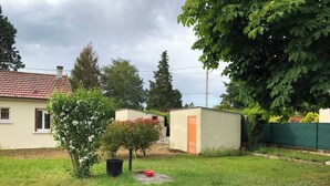Un patio cubierto de césped con un cobertizo pequeño, un árbol y una casa al fondo.