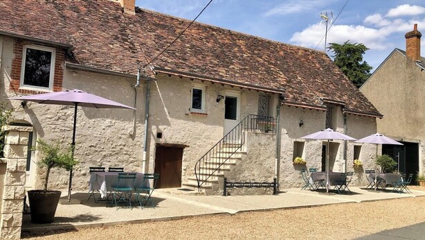 A rustic stone building with a tiled roof, outdoor seating with umbrellas, and a staircase leading to the entrance. - 1. Les gîtes de Joséphine Gîte a Chateau de la loire (Courbouzon)
