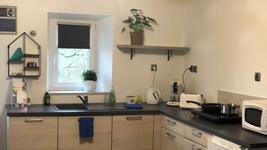 A modern kitchen with a built-in dishwasher, a microwave, and a kettle. There is a window with a view of trees outside. - 1. Les gîtes de Joséphine Gîte a Chateau de la loire (Courbouzon)