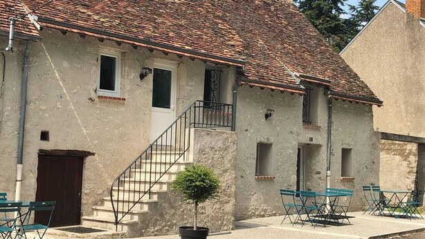 Un bâtiment rustique avec un toit en tuiles, un petit escalier et des sièges à l’extérieur.