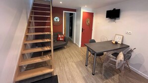 Un intérieur moderne avec un escalier en bois, un coin repas comprenant une table et des chaises, un canapé et un téléviseur fixé au mur.