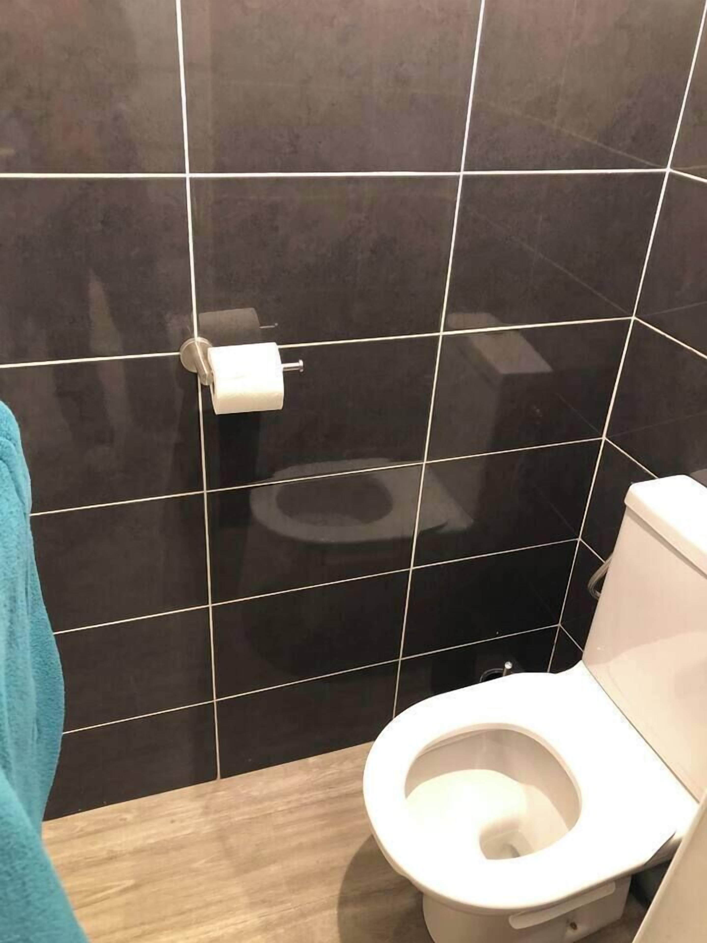 Een badkamer met zwart betegelde wanden, een wit toilet en een blauwe handdoek aan de linkerkant.