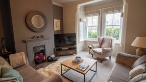 A living room with a fireplace, a television, and a comfortable seating area with a sofa and armchairs. - Refurbished Victorian House (Colchester)