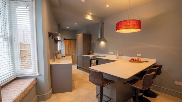 A modern kitchen with a central island, bar stools, and a red pendant light. - Refurbished Victorian House (Colchester)