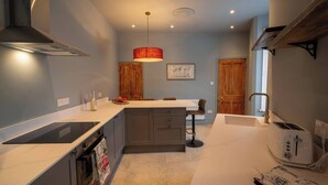 A modern kitchen with a built-in oven, a sink, and a toaster. There is a wooden cabinet and a hanging light fixture. - Refurbished Victorian House (Colchester)
