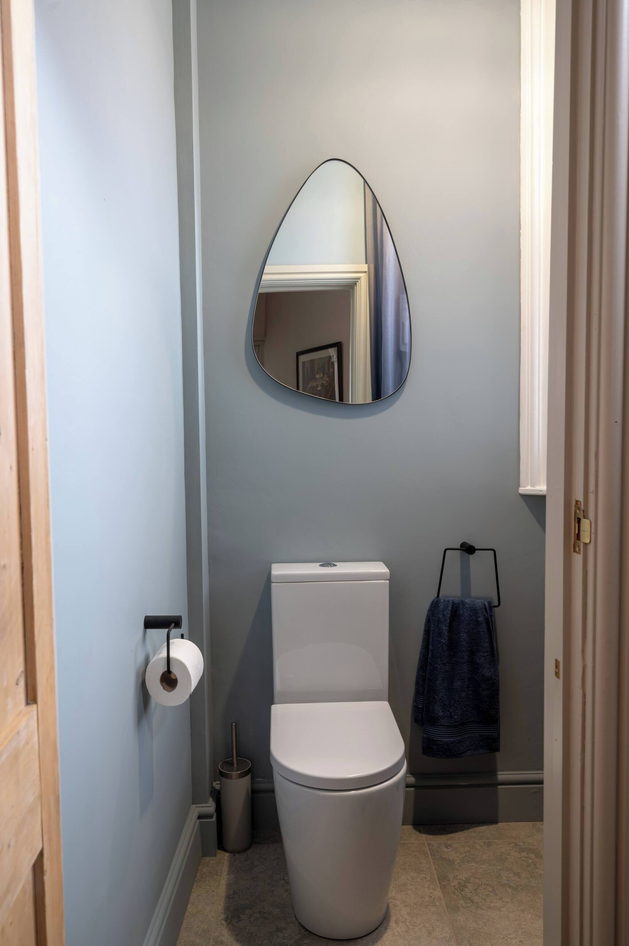 A bathroom with a toilet, a mirror, a towel rack, and a toilet paper holder.