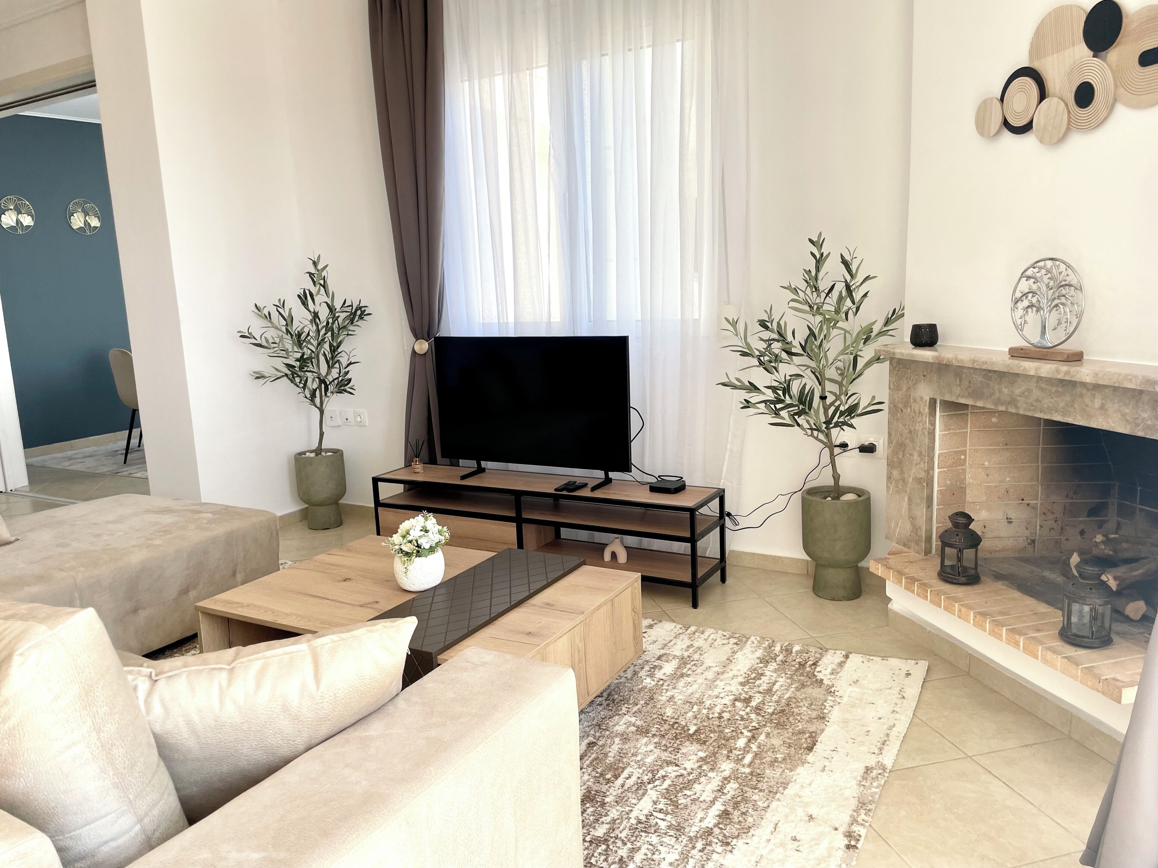 A modern living room with a flat-screen TV, a fireplace, and two potted plants.