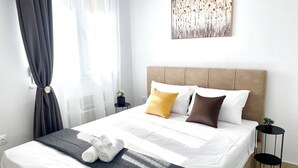 A neatly made bed with white and black bedding, a headboard, and a painting above it.
