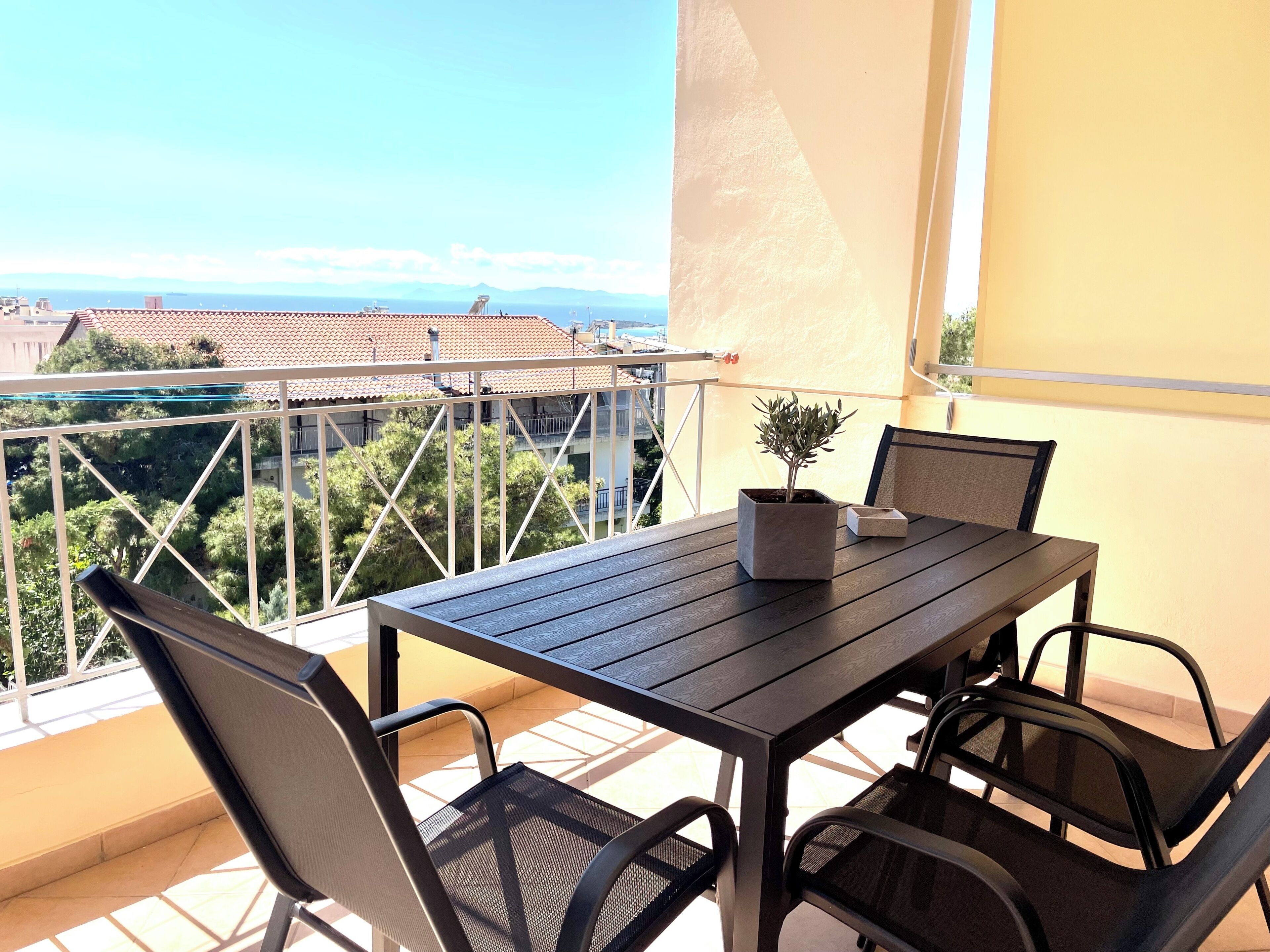 Un balcon avec une table et des chaises, un pot de fleurs et une vue sur la mer et les bâtiments.