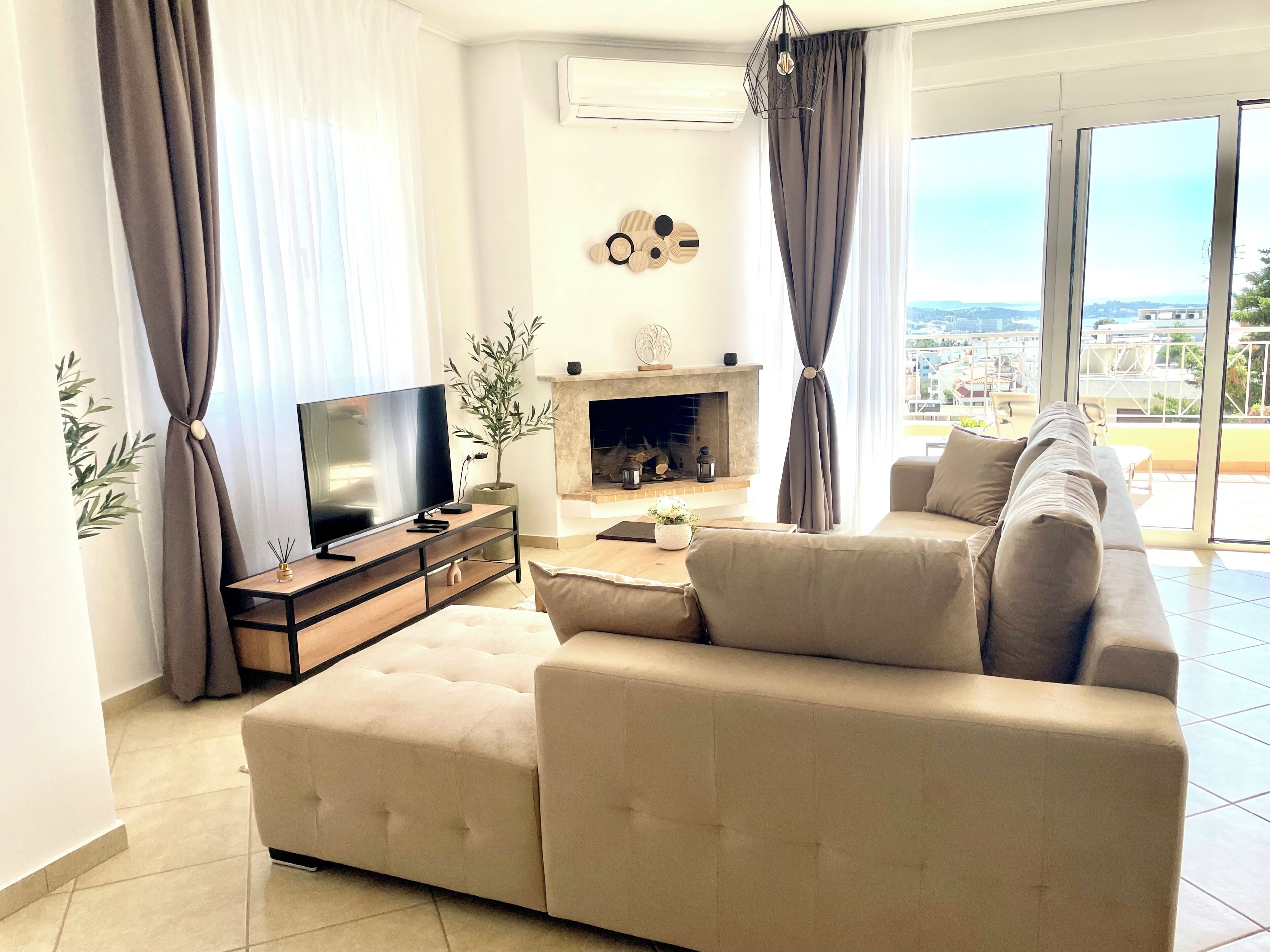 A modern living room with a sofa, TV, fireplace, and large windows offering a city view.