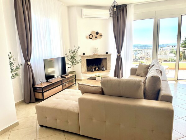 Uma sala de estar moderna com sofá, TV, lareira e grandes janelas com vista para a cidade.