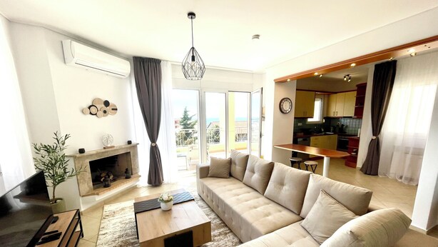 A modern living room with a sectional sofa, a fireplace, and a view of the kitchen and balcony.