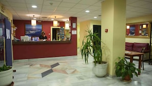 A hotel reception area with a marble floor, a receptionist desk, potted plants, and a seating area with a couch and chairs. - Hotel Olas de Almuñécar (Almuñécar)