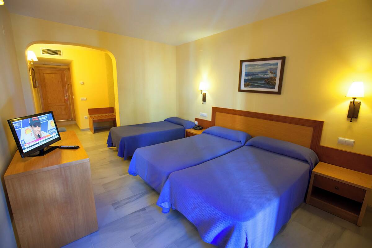Hotellihuone, jossa on kaksi sänkyä, televisio puupöydällä ja taulu seinällä.