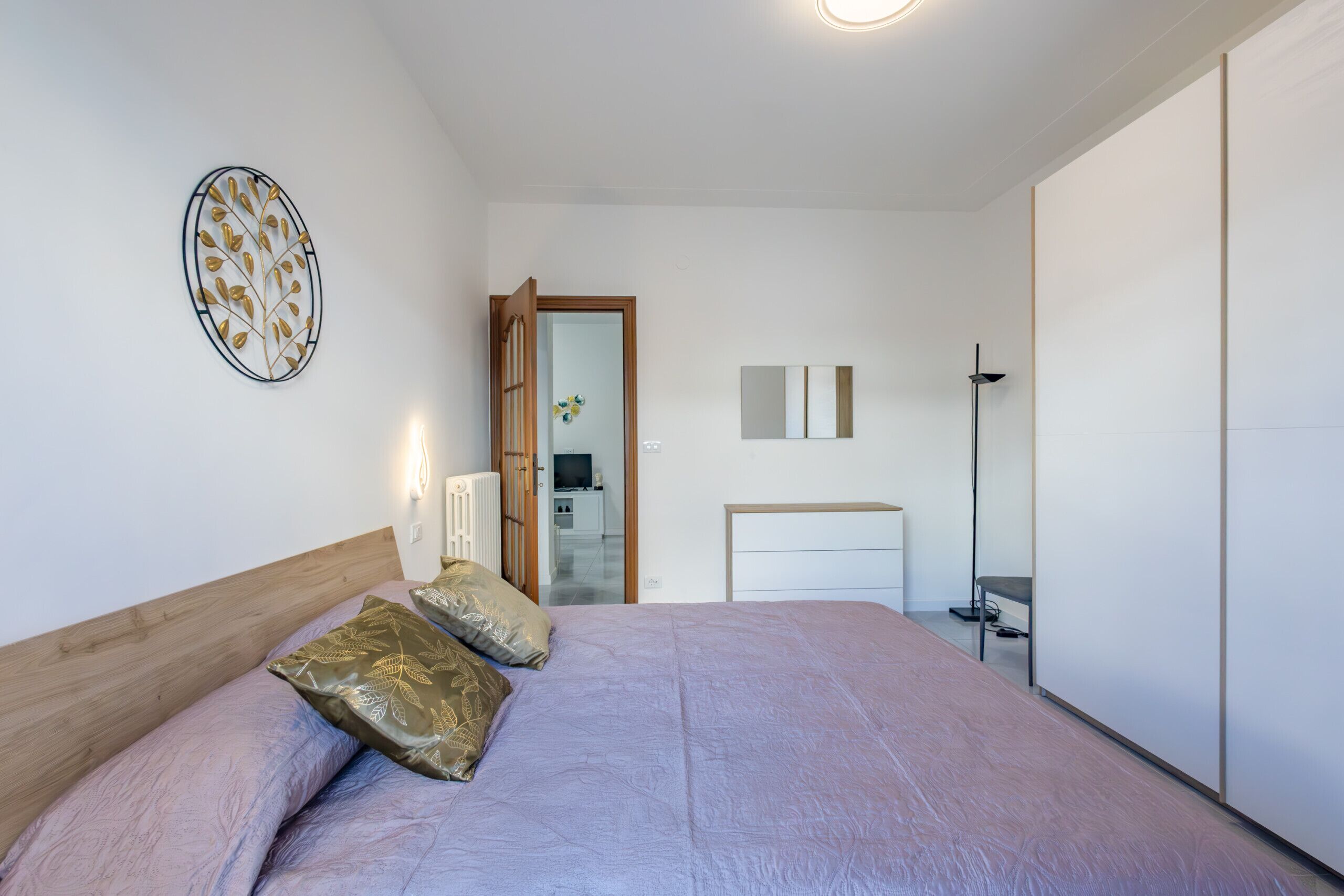 A bedroom with a bed, pillows, a bedside table, a mirror, and a wardrobe.