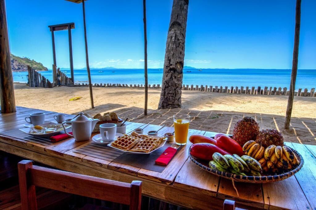 A wooden table with breakfast items and a view of the beach.