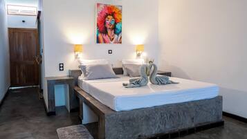 A bedroom with a bed, bedside lamps, a painting, and a wooden door.