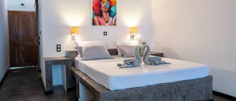 A bedroom with a bed, bedside lamps, a painting, and a wooden door.