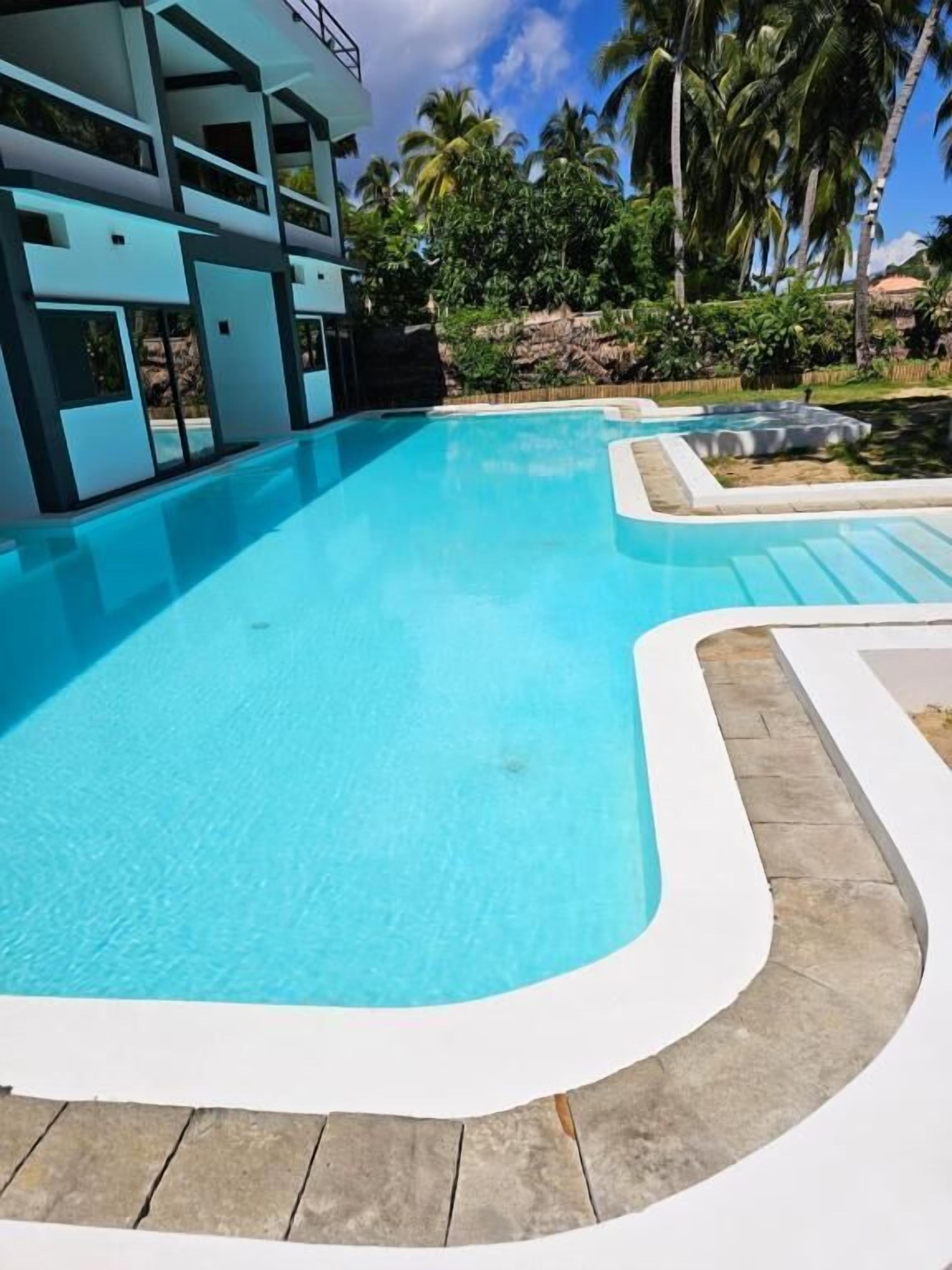 Una piscina junto a un edificio moderno, rodeada de palmeras y follaje.
