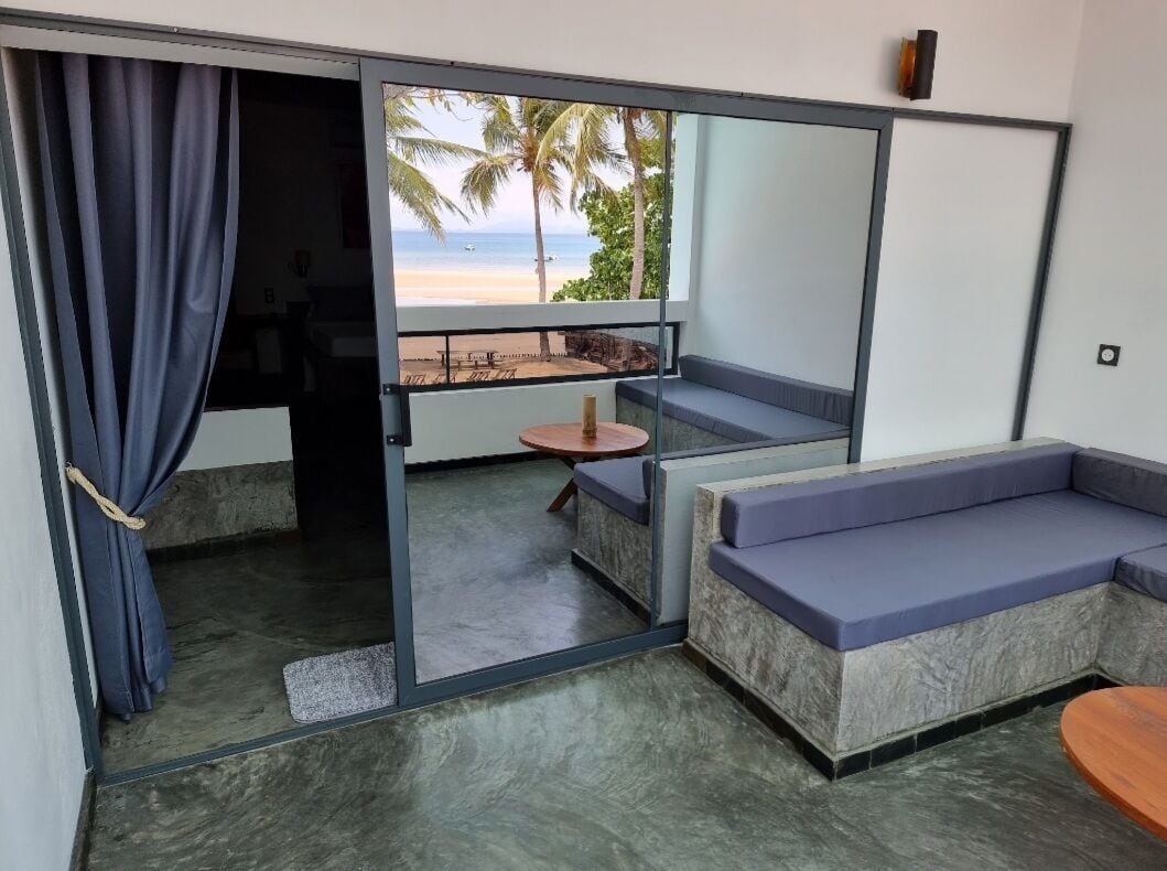 A room with a sliding glass door leading to a balcony with a beach view, a small round table, and a sofa.