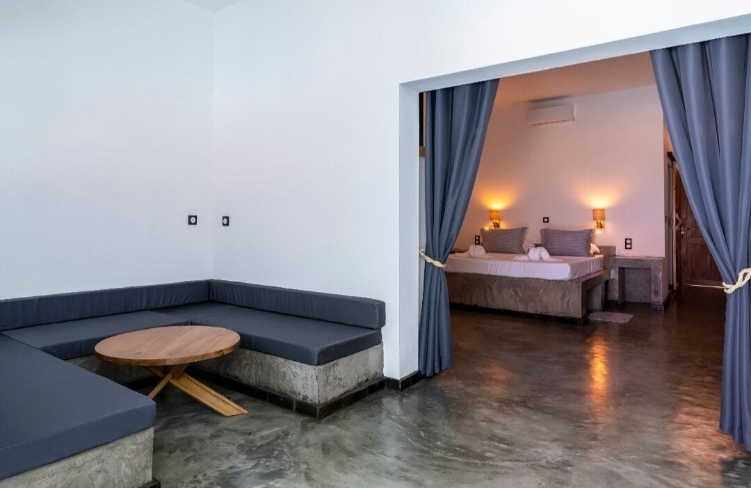 A modern room with a sectional sofa, a round wooden table, and a bed with a headboard.