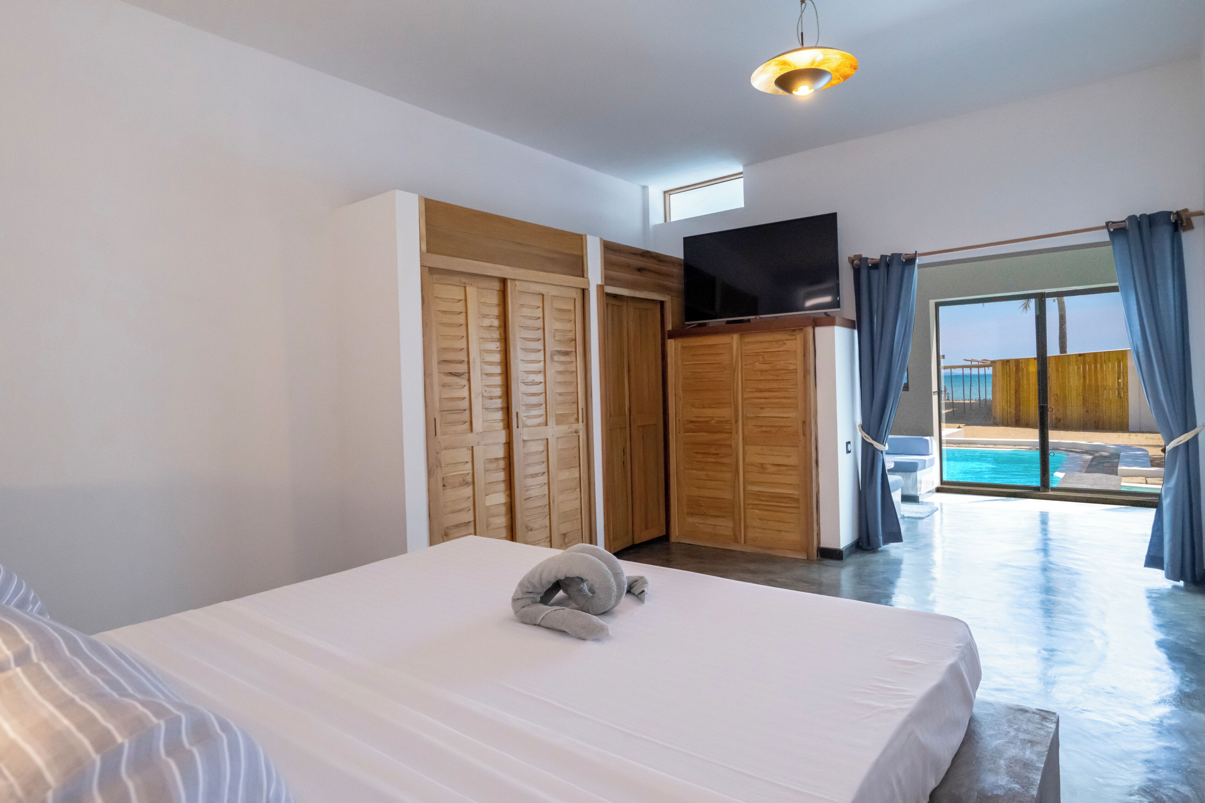 A bedroom with a bed, a television, wooden closets, and a view of a pool.