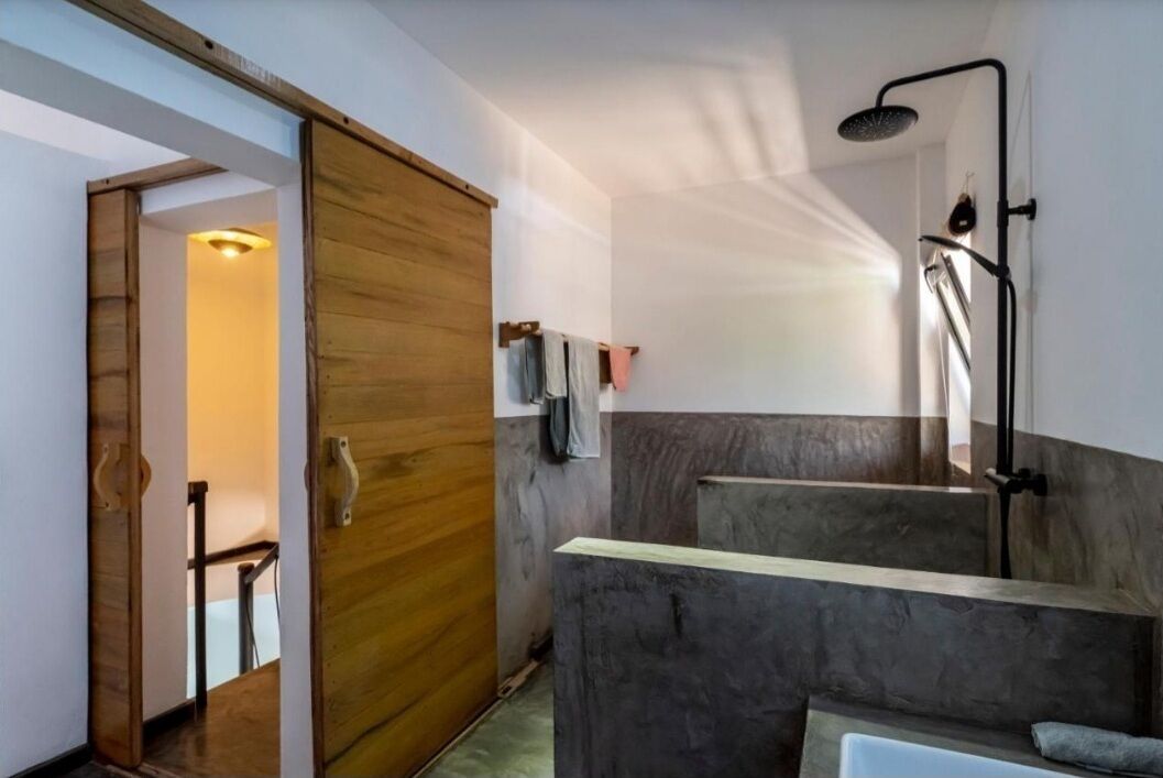 A modern bathroom with a shower, a wooden door, and a view of a hallway.