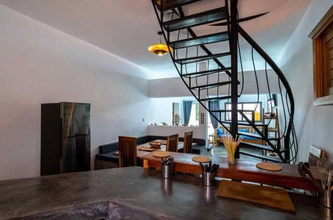 A modern kitchen with a spiral staircase, wooden dining table, and chairs.