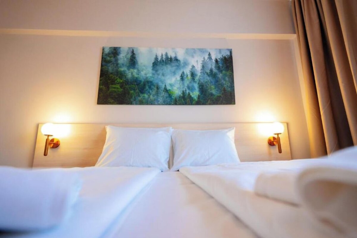 A hotel room with a bed, two bedside lamps, and a painting above the bed.