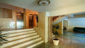 Eine Hotelhalle mit Marmorboden, einer Treppe, einem Empfangstresen und einer Sitzecke.