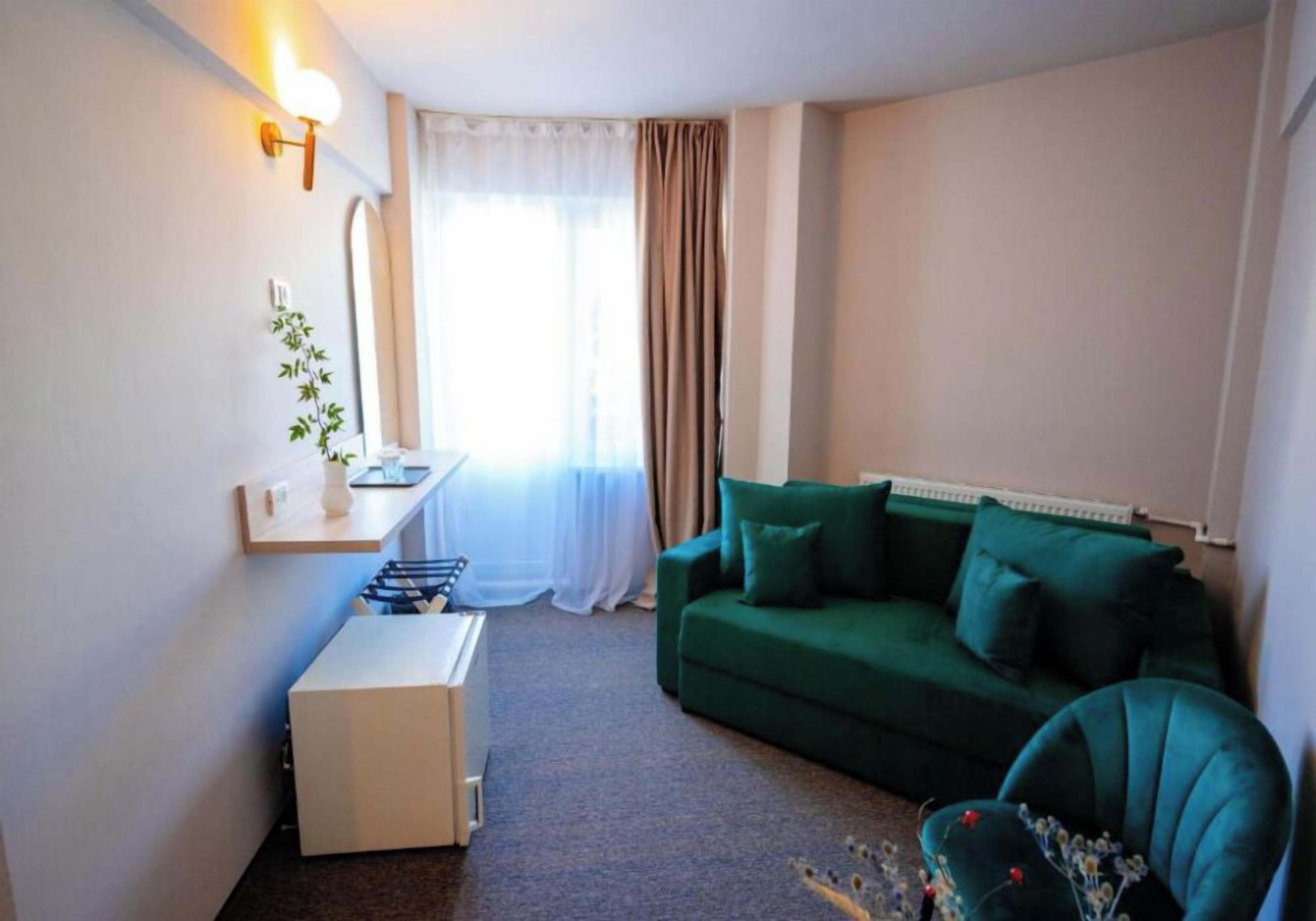 A small, well-lit room with a green sofa, a white side table, and a radiator.