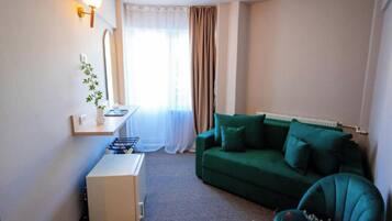 A small, well-lit room with a green sofa, a white side table, and a radiator.