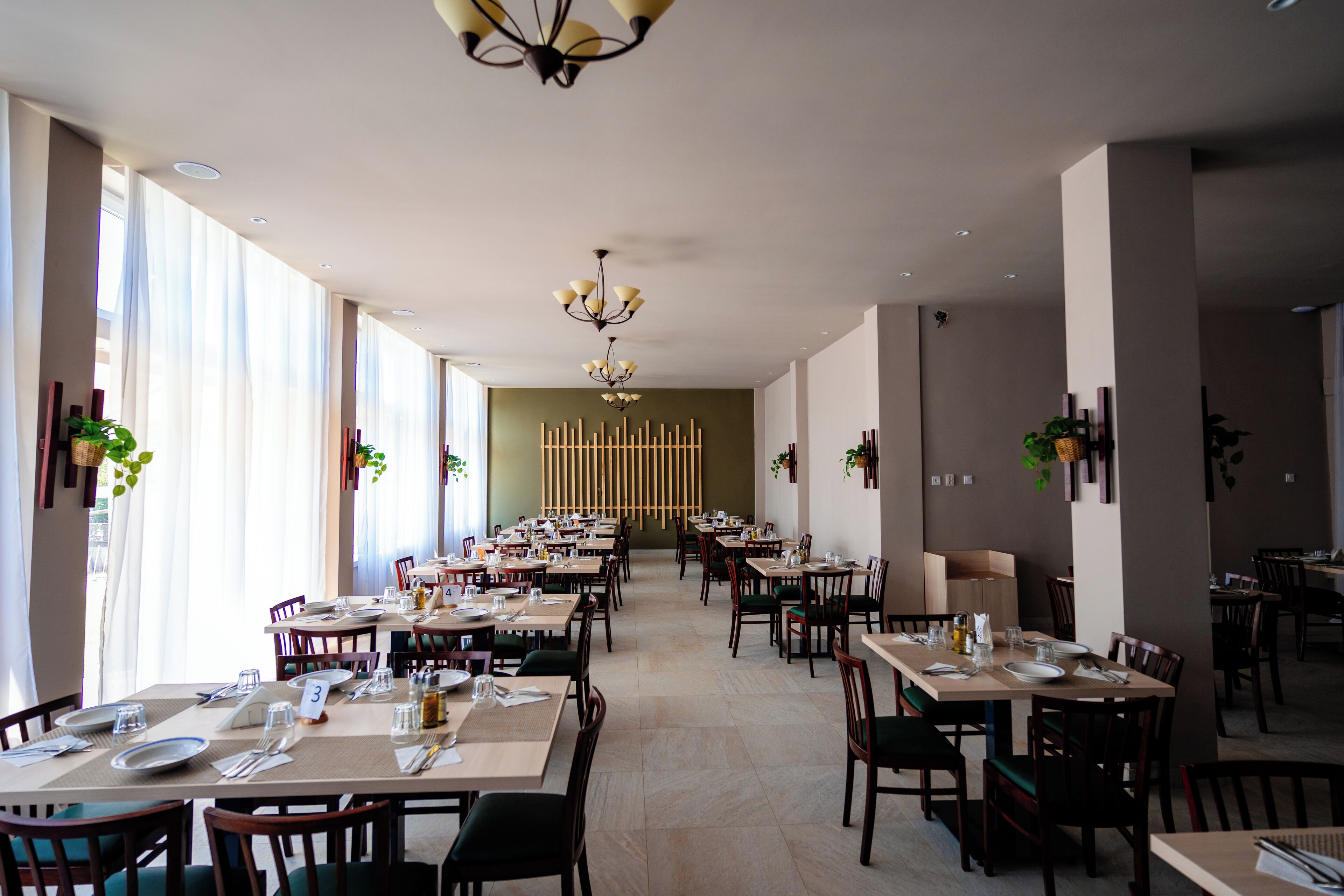 Ein geräumiges Restaurant mit mehreren Tischen, Stühlen, großen Fenstern und einem modernen Kronleuchter.