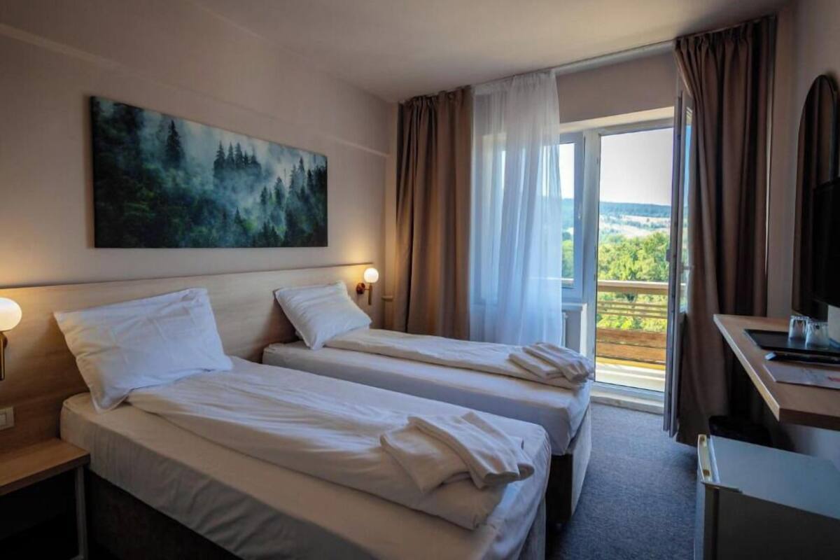 Habitación de hotel con dos camas, un cuadro en la pared, un escritorio con una silla y vistas al exterior.