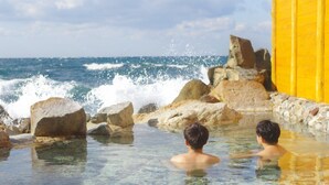 A clear pool with two people swimming, surrounded by large rocks and a yellow wall.