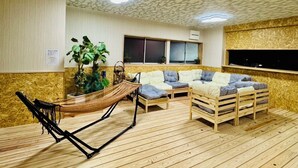 A room with a wooden floor, a hammock, a sofa, and a window.
