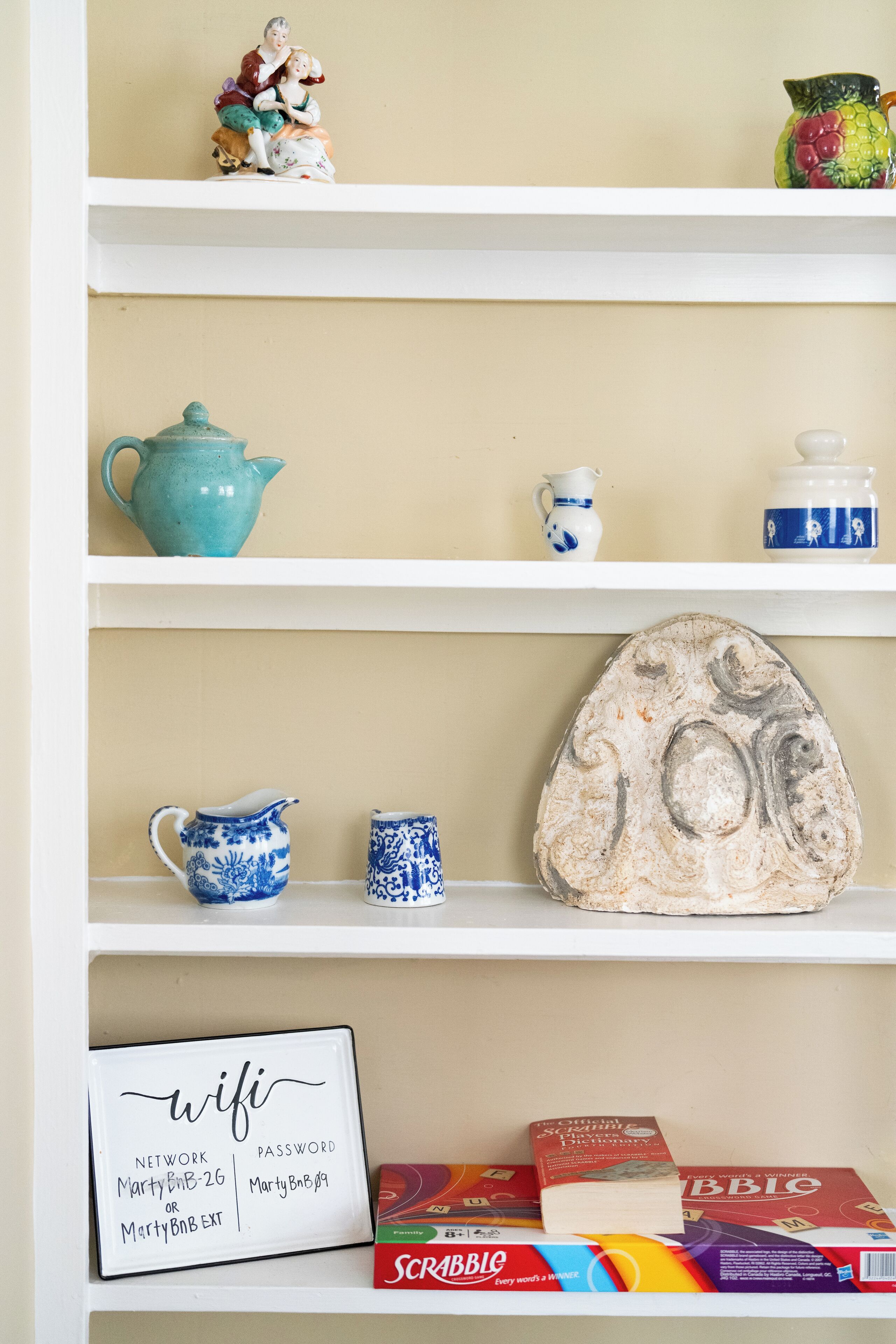 A shelf with decorative items including a ceramic teapot, a ceramic jug, a ceramic pitcher, a ceramic mug, a ceramic plate, and a framed sign with wifi information.