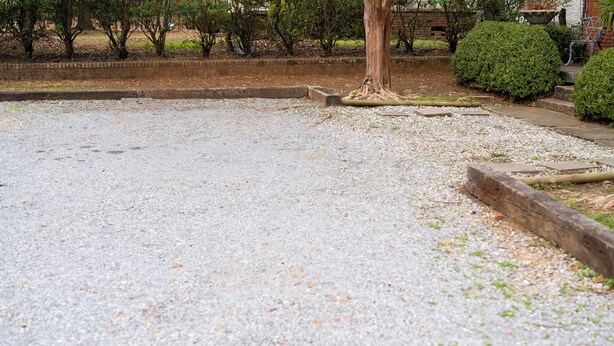 A gravel parking area with a tree and a small bush. - A surprisingly roomy, quiet Montgomery home base for families, pet travelers, and longer stays—minutes from downtown and Maxwell, with space to actually settle in. (Montgomery)