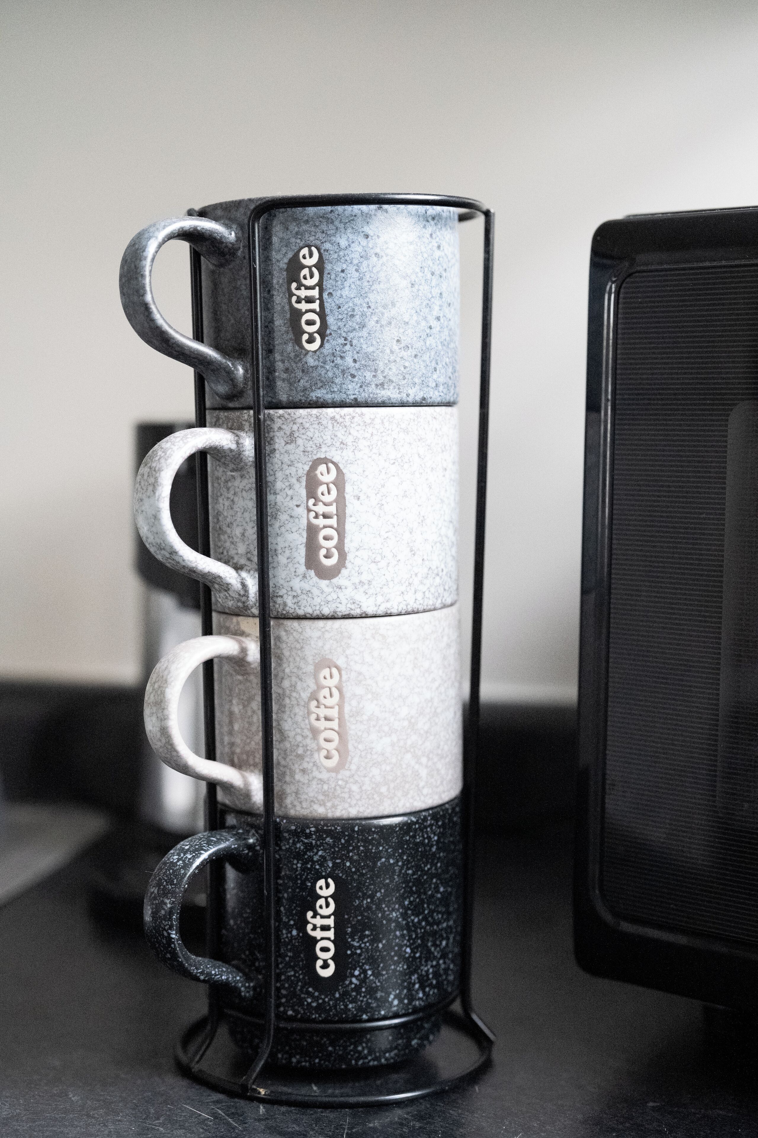 A stack of coffee mugs with the word "coffee" on them, placed next to a black speaker.