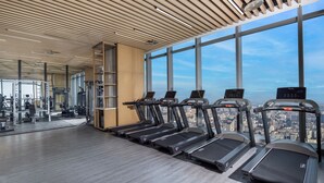 A gym with treadmills, weight machines, and a city view through large windows. - Jinmao Grandee Hotel Jiangyin Chengfa (Wuxi)