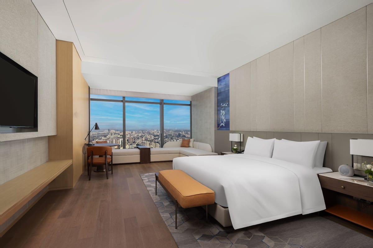 A modern hotel room with a large bed, a desk, a chair, and a TV.